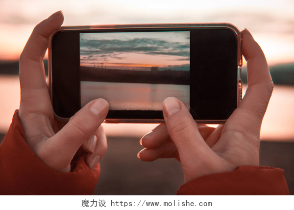 一个女人拿着手机在拍风景妇女手拿着手机, 照片上有山湖风景.